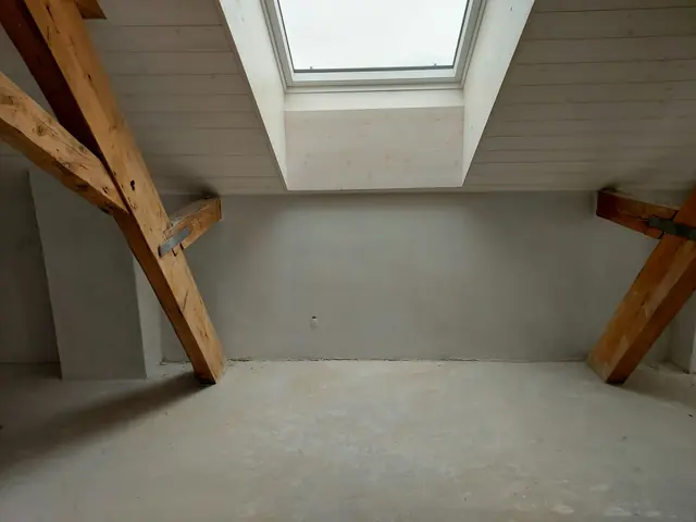 Attic under renovation with exposed beams and roof window